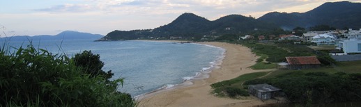 Landscape photo of a waterfront community on a Brazilian beach. Multiple buildings lie between a sandy beach berm and the background of tall mountains.
